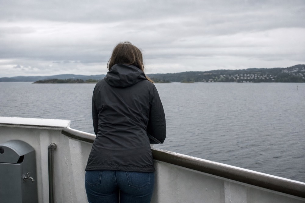 A person in jeans and a rain jacket standing at an Oslofjord railing on an overcast day, no text, no logos, no people