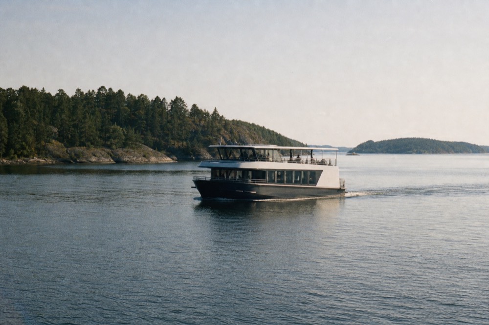 A silent electric cruise boat gliding across calm Oslofjord water near forested islands, no text, no logos, no people.