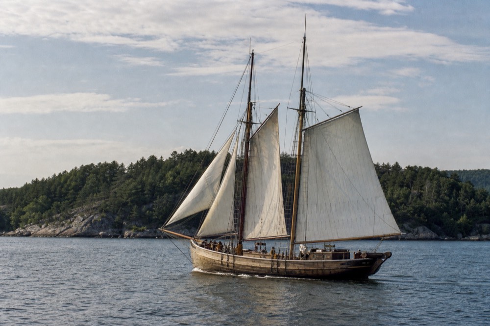A traditional wooden sailing ship underway on the Oslofjord with green islands behind it, no text, no logos, no people.
