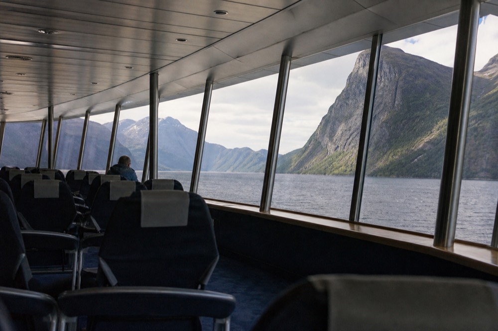 A glass-walled panorama lounge inside a cruise ship with fjord scenery through the windows, no text, no logos, no people.