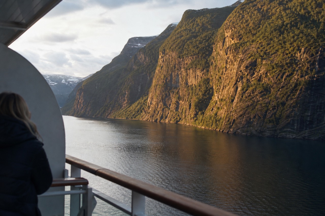 A cruise ship balcony overlooking steep Norwegian fjord cliffs at golden hour, no text, no logos, no people.