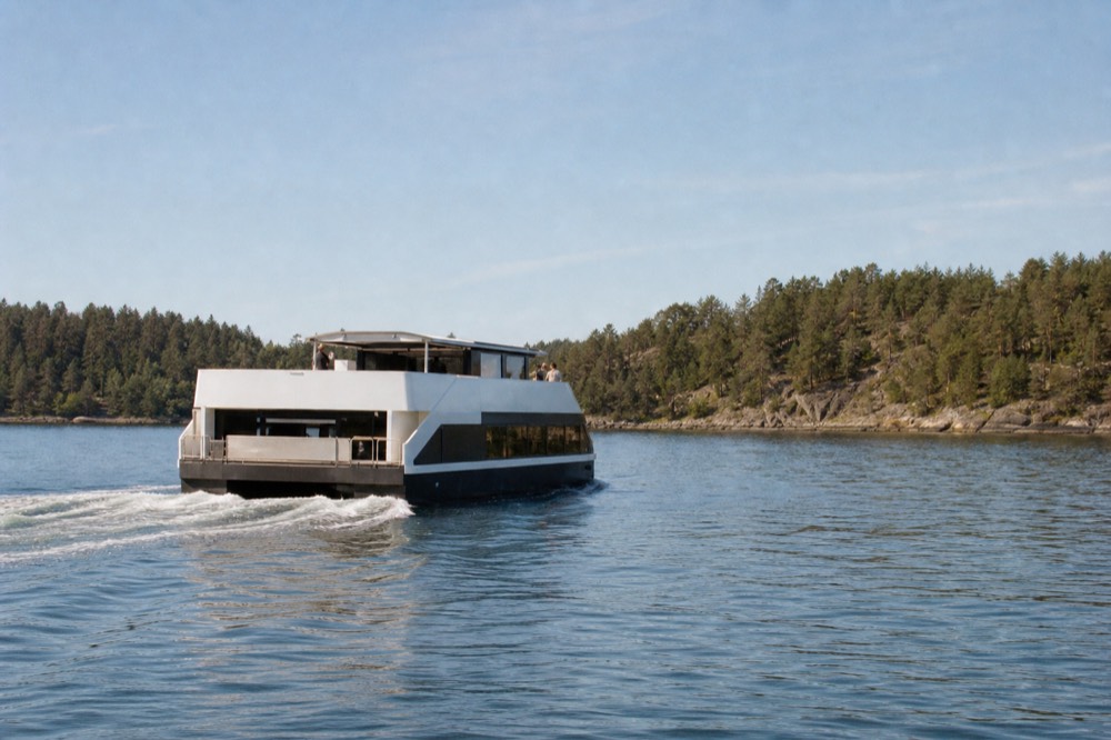 A silent electric cruise boat gliding across calm Oslofjord water near green islands, no text, no logos, no people.
