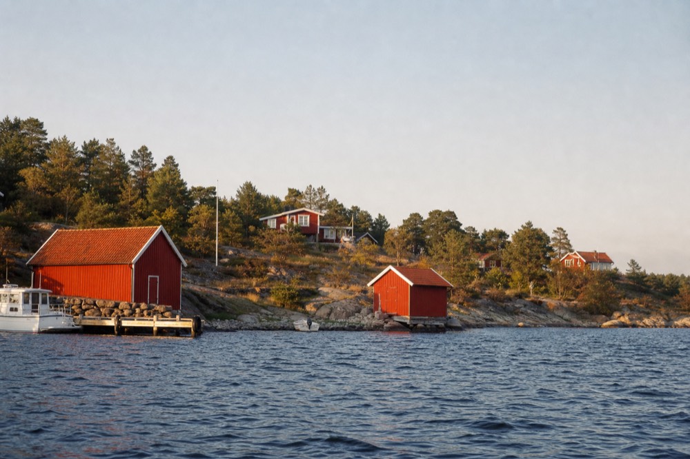 Red summer cabins on a small green Oslofjord island seen from the water, no text, no logos, no people