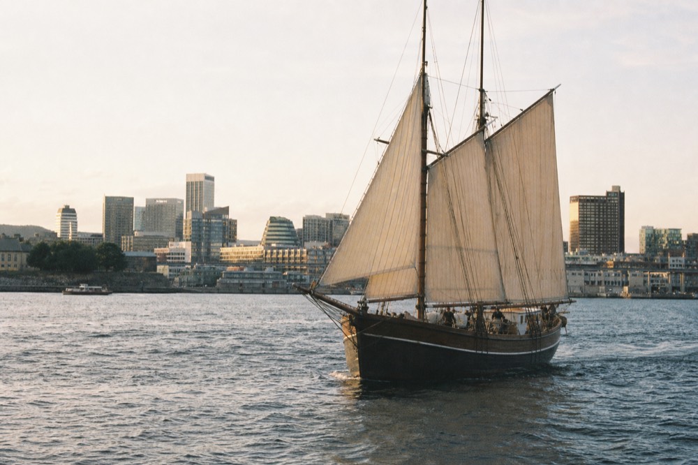 A traditional wooden sailing ship under way on Oslofjord with the city skyline behind, no text, no logos, no people