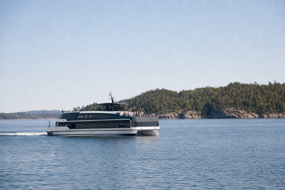 A silent electric cruise boat gliding across calm Oslofjord water near green forested islands, no text, no logos, no people.