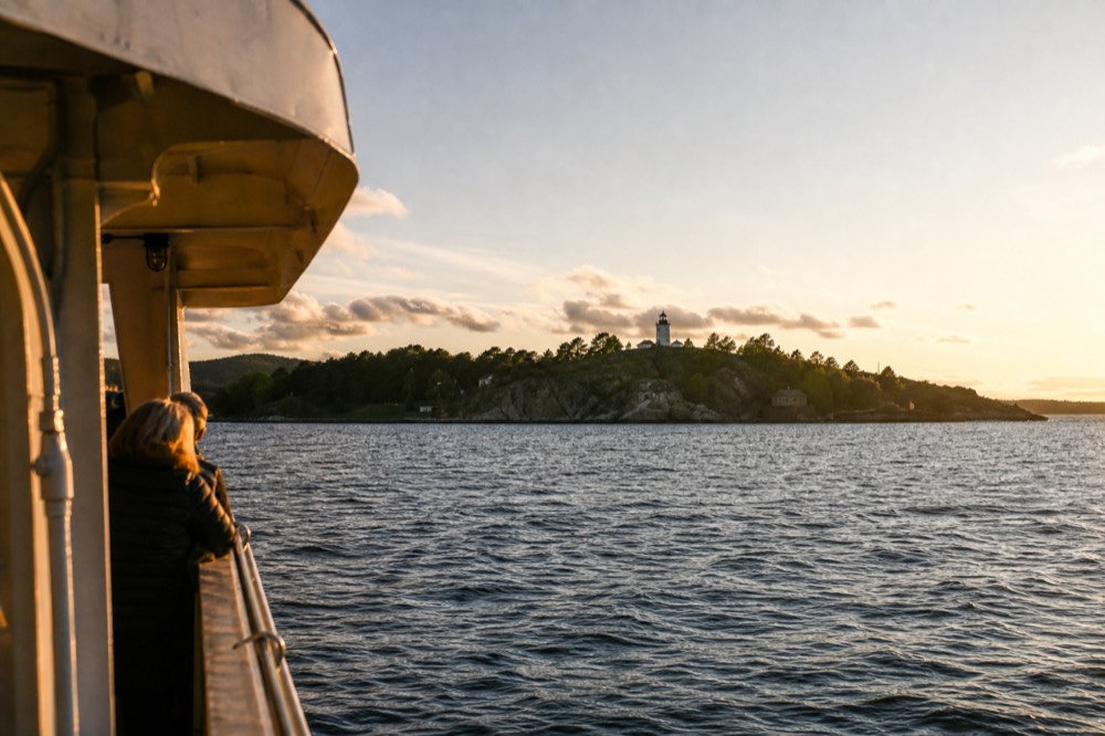 Green island with a small lighthouse in the Oslofjord seen from a boat deck at golden hour, no text, no logos, no people