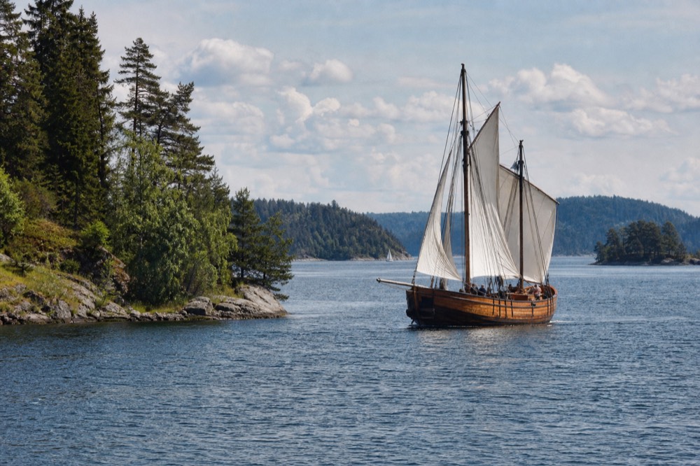 A wooden sailing ship cruising between forested fjord walls near Oslo, no text, no logos, no people