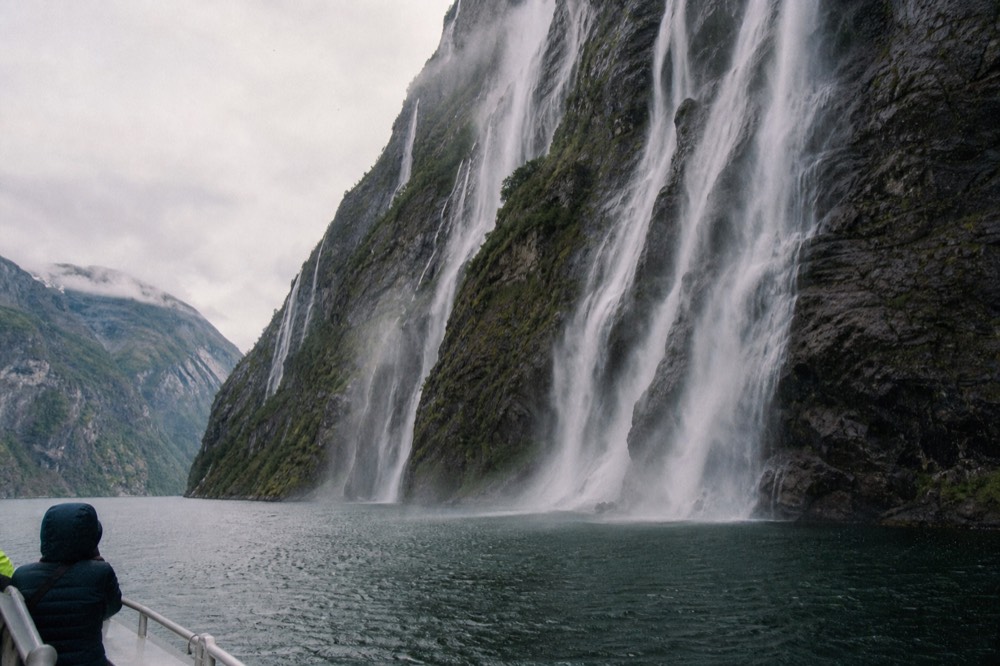 Waterfalls streaking down dark rock into a deep western Norwegian fjord, no text, no logos, no people